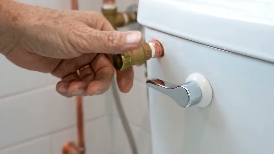 Hands turning a water valve behind a toilet