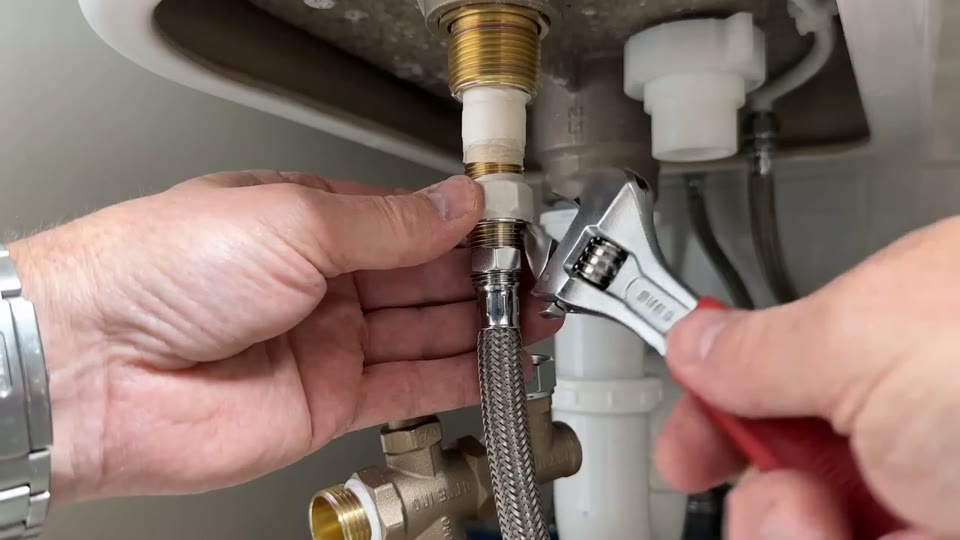Hands installing a brass T-valve on a toilet supply line