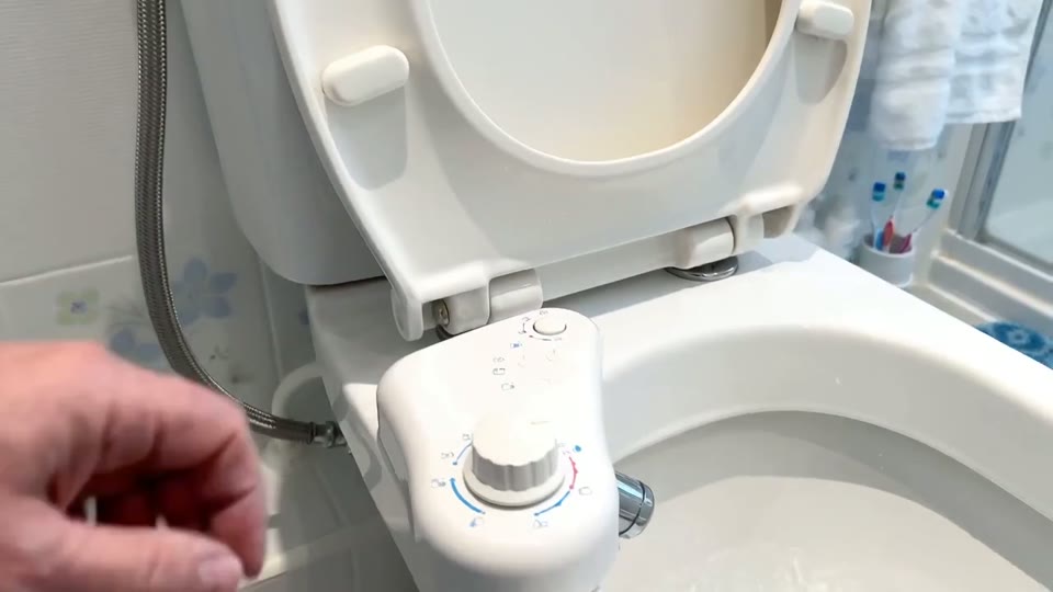 Hand testing bidet spray in a toilet bowl